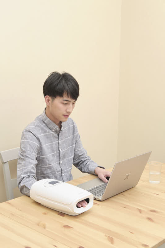 C20 Graphene Heated Hand Massager: man using the device beside a laptop.