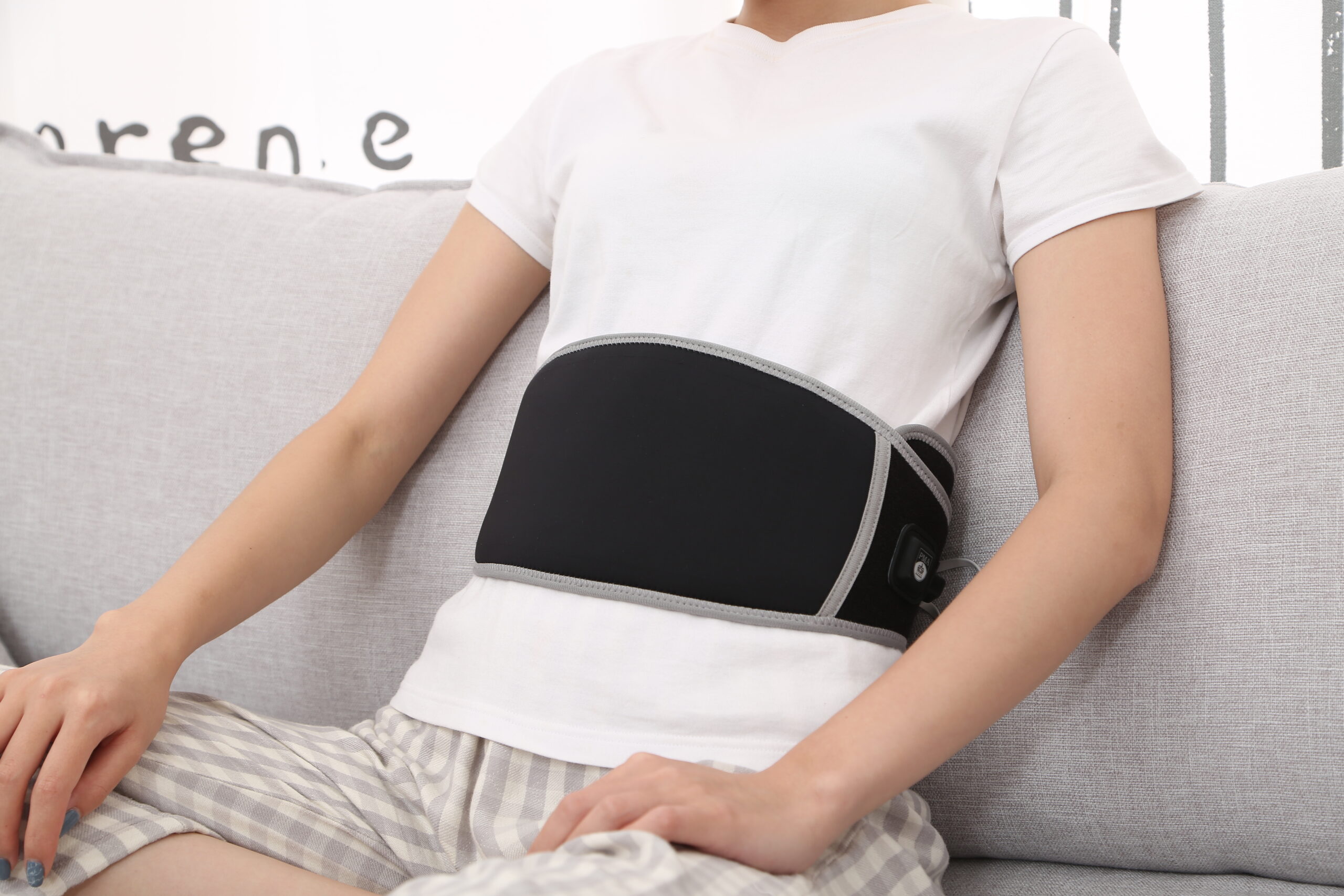 F10 Graphene Heating Salt & Herb Belt: woman seated on a sofa wearing the black belt.