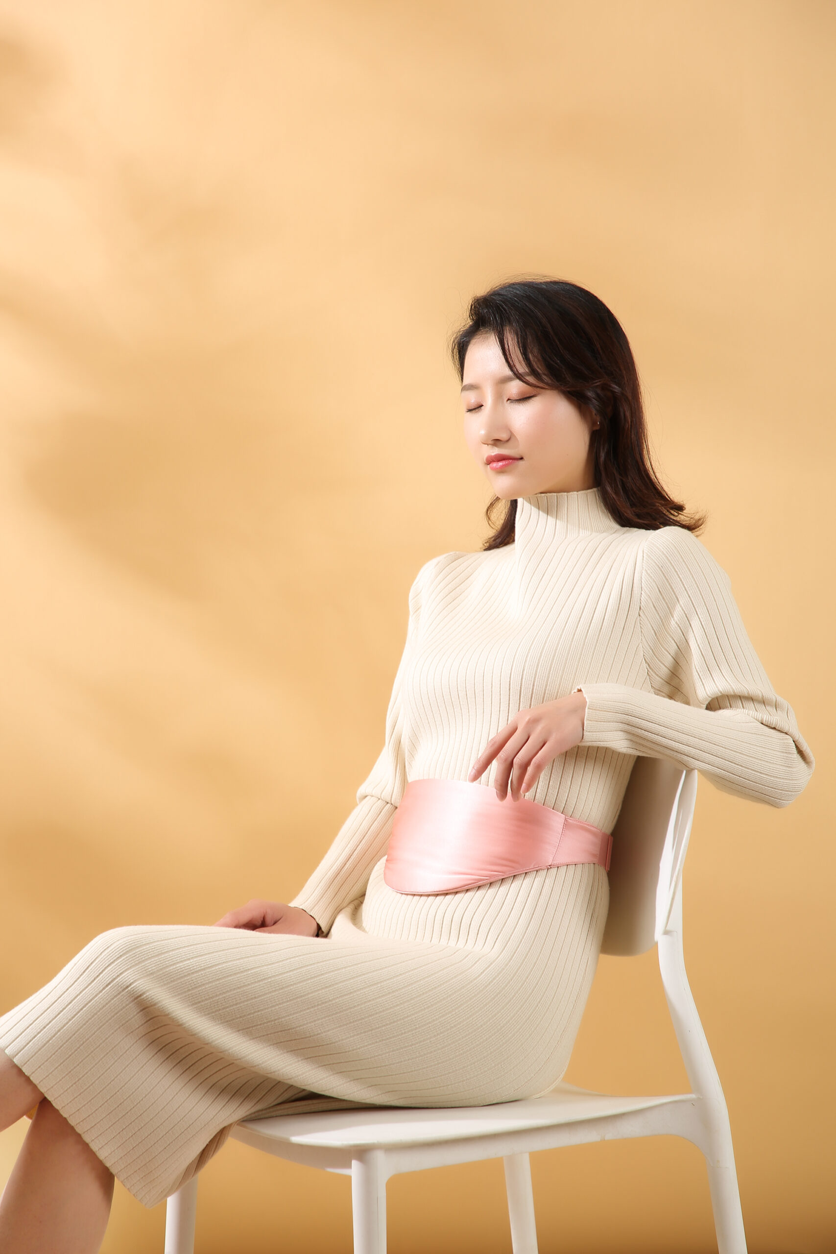 D10 Graphene Heated Silk Abdomen Belt: woman seated and adjusting the pink abdomen belt.
