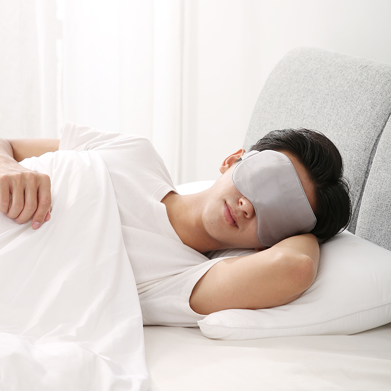 E10 Graphene Heated Silk Eye Mask: man resting in bed with the gray mask.