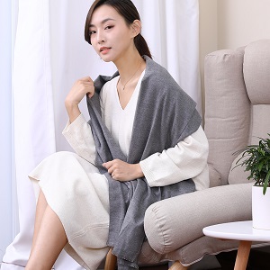 R10 Graphene Heated Scarf: gray scarf worn as a shawl while seated.