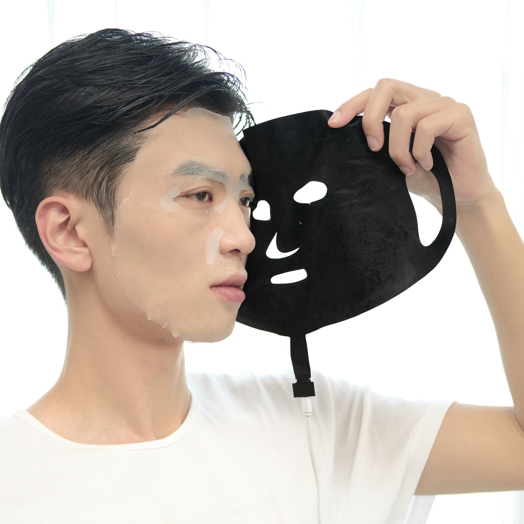 X10 Graphene Heated Face Mask: man holding the black mask beside his face.