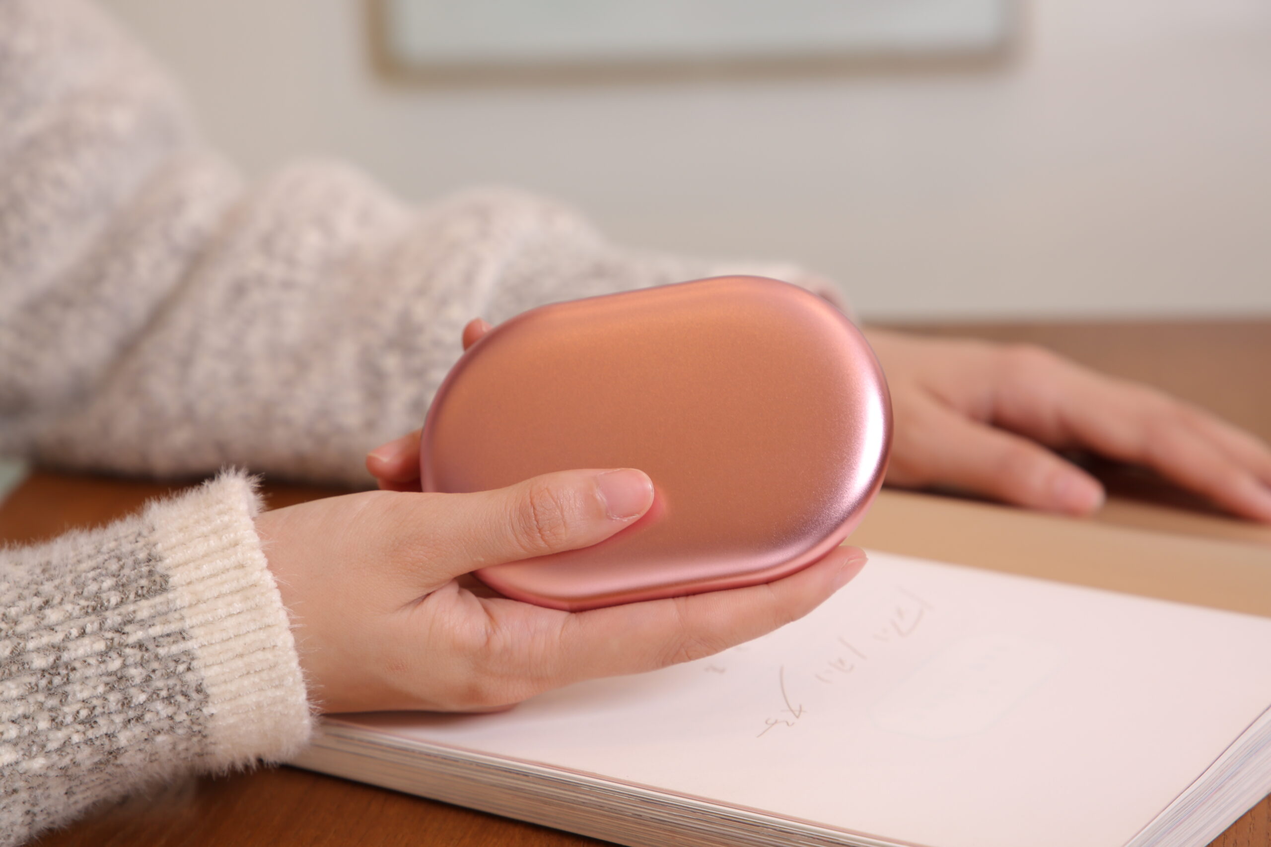 Z20 Graphene Heated Hand Warmer: hand holding the pink warmer over a notebook.