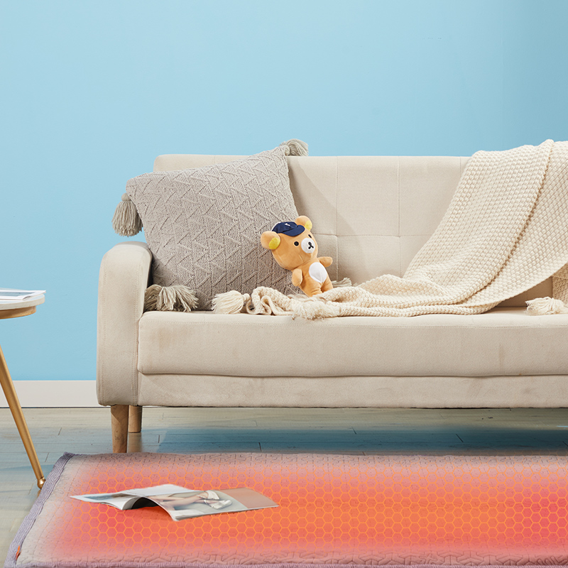Graphene Electric Blanket: blanket displayed as a floor mat beside a sofa.